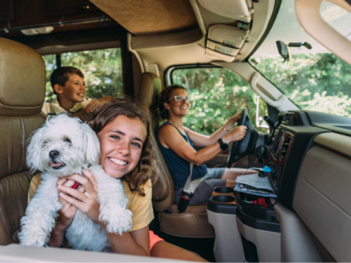 a girl holding a white dog while her mom drives the rv they secured with an RV Loan from Essential Credit Union in HOuston