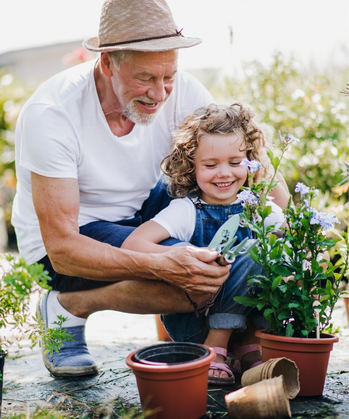 A grandfather in a fedora helping his granddaughter care for a small potted plant